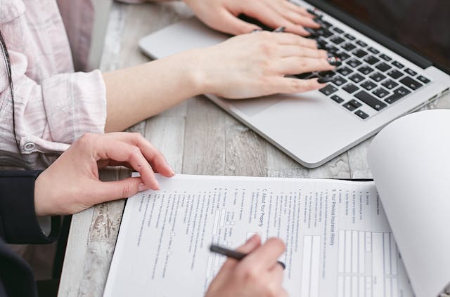 Person filling out a form next to another person on a laptop